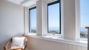 Ein Zimmer mit einem Korbstuhl und Meerblick durch zwei Fenster.
