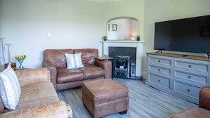 Un salon avec un canapé en cuir marron, un pouf assorti, un meuble en bois gris et un téléviseur à écran plat.