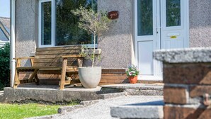 Une maison avec une façade en pierre, un banc en bois, un grand pot de fleurs et une porte sur laquelle est affiché un panneau avec le mot « Sourire ».