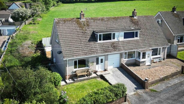 Une maison à deux étages, dotée d’un toit en pente, d’un porche à l’avant et d’un petit jardin.