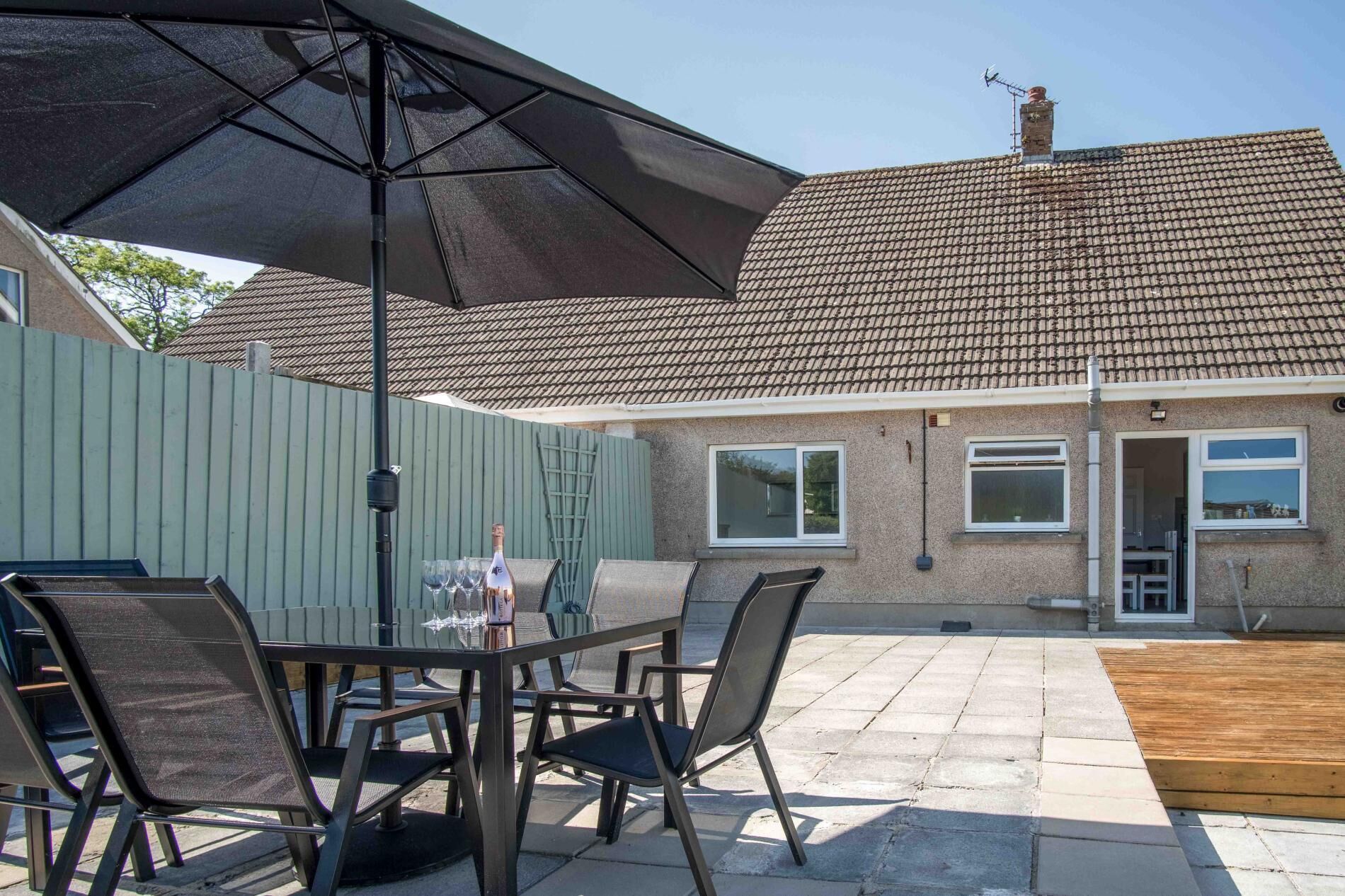 An outdoor patio with a table and chairs, a large umbrella, and a house in the background.