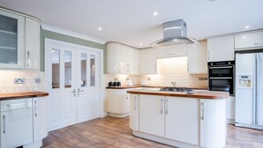 A modern kitchen with white cabinetry, a central island, and built-in appliances. - Ridgeway Meadow Bungalow - 3 Bedroom - Manorbier (Tenby)