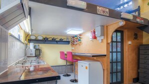 A compact kitchen with a gas stove, a small refrigerator, and a pink chair. - Clouds - 1 Bedroom Holiday Home - Milford Haven (Milford Haven)
