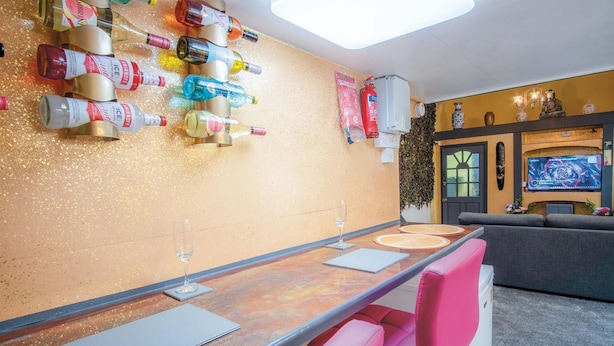 A bar area with a long counter, multiple bottles of beverages, a fire extinguisher, and a television screen in the background. - Clouds - 1 Bedroom Holiday Home - Milford Haven (Milford Haven)