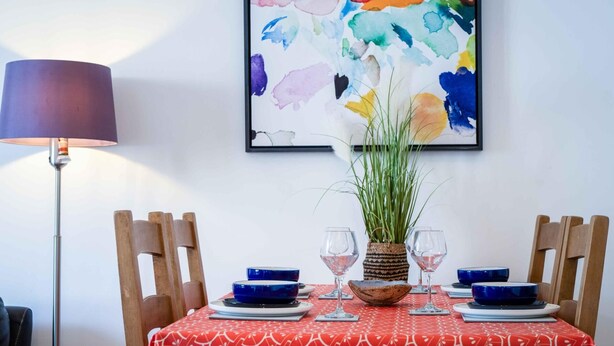 Uma mesa de jantar com toalha de mesa estampada em vermelho, tigelas azuis, copos de vinho e uma cesta de palha.