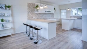 A modern kitchen with a central island, bar stools, pendant lighting, and a backsplash with mosaic tiles. - Longview - 4 Bedroom Holiday Home - Pembroke Dock (Pembroke Dock)