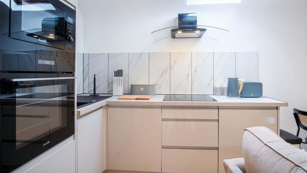 A modern kitchen with a built-in oven, a microwave, and a stove. There is a window above the sink, and a small window on the left side.