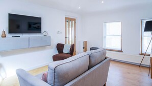 A modern living room with a flat-screen TV, a sofa, a chair, a window, and a radiator.