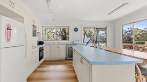 A modern kitchen with white cabinets, a built-in oven, and a large island with a blue countertop. - Ocean Echoes - Pet Friendly with Ocean Glimpses (Culburra Beach)