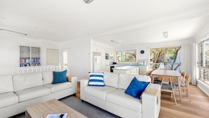 A modern living room with a sofa set, a coffee table, and a dining area with a table and chairs. - Ocean Echoes - Pet Friendly with Ocean Glimpses (Culburra Beach)
