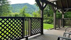 Eine überdachte Terrasse im Freien mit Gittergeländer, Holzboden und Blick auf eine gebirgige Landschaft.