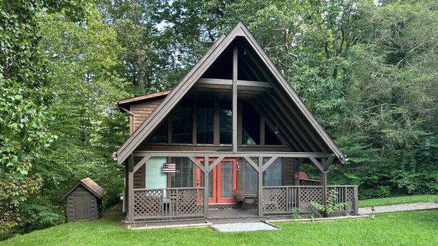 Eine Holzhütte mit Veranda und einer kleinen Scheune in einem Waldgebiet.