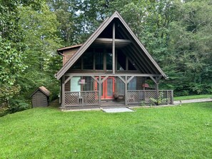 Eine Holzhütte mit Veranda und einer kleinen Scheune in einem Waldgebiet.