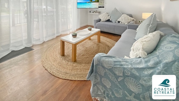 En stue med TV, sofa, sofabord og havudsigt gennem store vinduer.