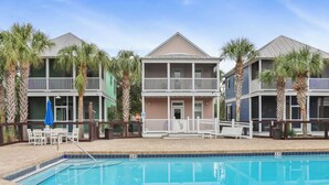 A poolside area with a pool, a two-story building with balconies, and palm trees. - Seabbatical | Pet-Friendly Cottage | Screened Decks + Community Pools 🐾 (Port St. Joe)