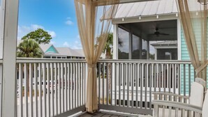 A covered porch with a white railing, a white chair, and a view of a house with a teal roof. - Seabbatical | Pet-Friendly Cottage | Screened Decks + Community Pools 🐾 (Port St. Joe)