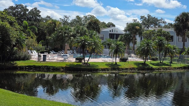 Un área de piscina con sillones de descanso, un estanque pequeño y un edificio de fachada blanca.