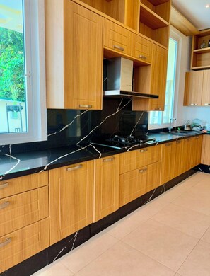 A modern kitchen with wooden cabinets, a black marble countertop, and a built-in stove. - Sea View Luxury Mansion • Pool & Jacuzzi (Koh Chang)