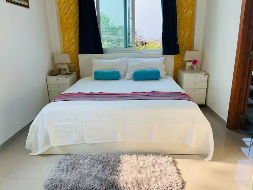 A bedroom with a bed, two bedside tables, a window with curtains, and a rug.