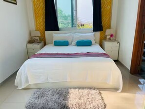 Un dormitorio con cama, dos mesitas de noche, una ventana con cortinas y una alfombra.