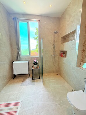 Un baño con ducha, inodoro, toallero, una mesita con planta y una ventana con cortinas.