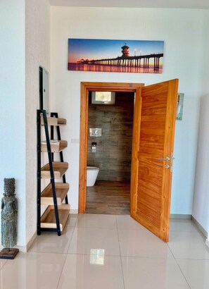 Un interior moderno con una puerta de madera que da a un baño, una escalera y un cuadro de un muelle.