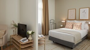 A hotel room with a bed, a desk with a phone, a TV, and a vase with flowers. - Zenao Appart'hôtels Marseille Prado (Marseille)