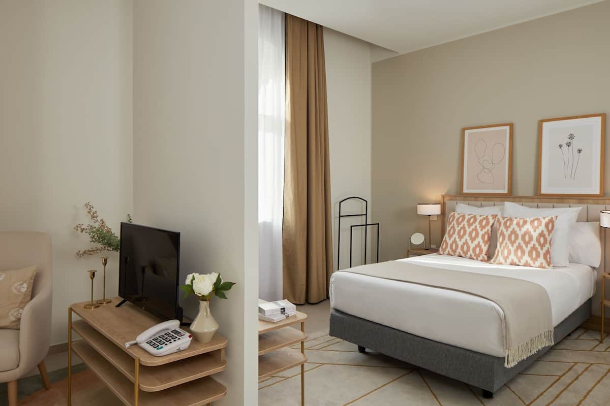 A hotel room with a bed, a desk with a phone, a TV, and a vase with flowers.