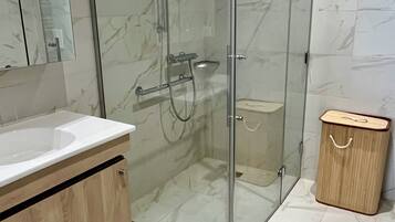 Un baño moderno con ducha envuelta en vidrio, tocador de madera y suelo de mármol.