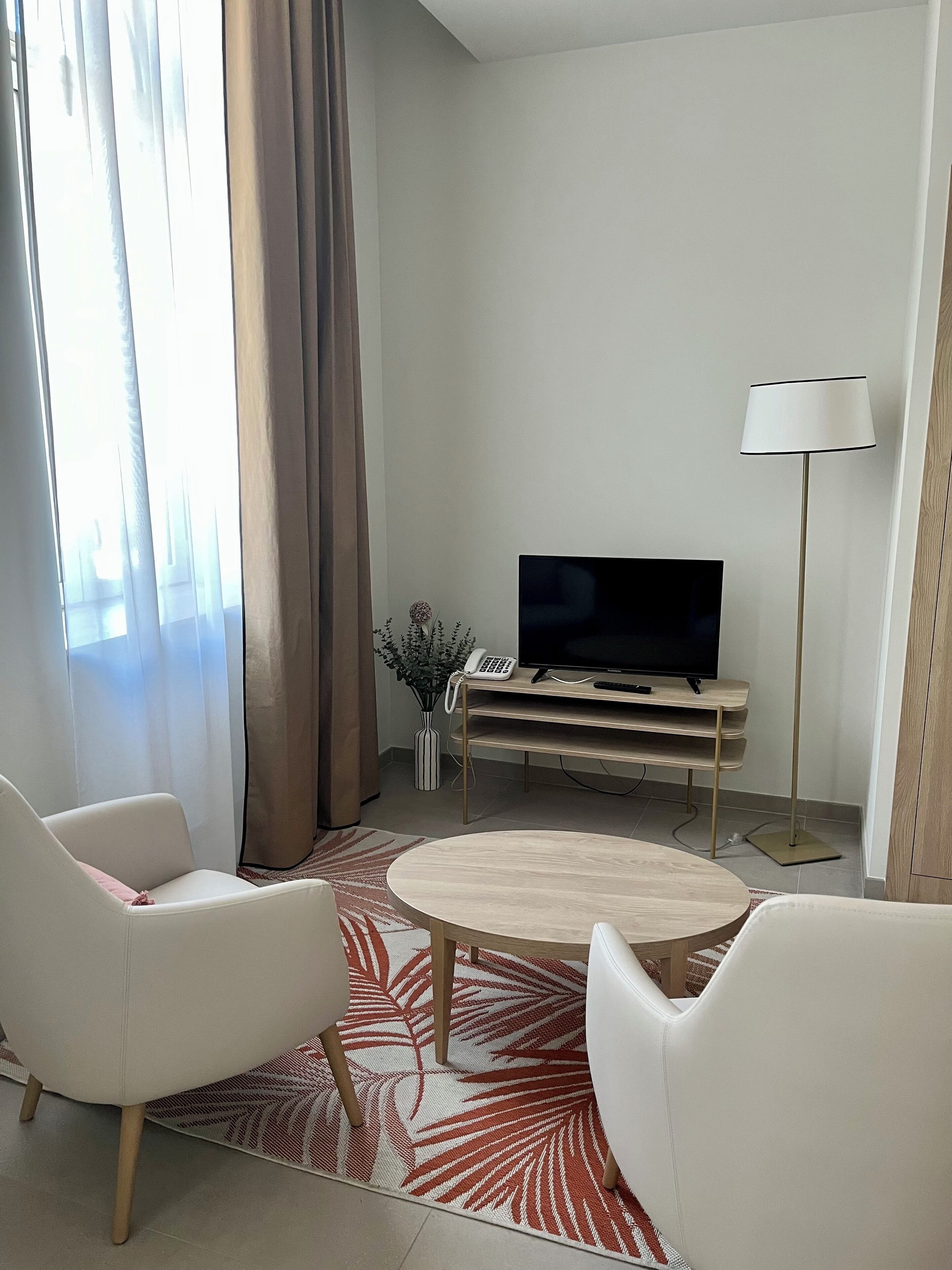 Ein modernes Wohnzimmer mit Flachbildfernseher, zwei weißen Sesseln, einem Couchtisch und einer Stehlampe.