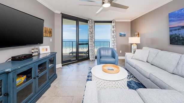 A living room with a TV, a sofa, a chair, a coffee table, and a balcony with a view.