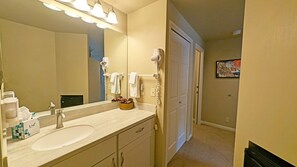 A bathroom with a sink, mirror, and hairdryer. There is a towel rack and a door leading to another room.