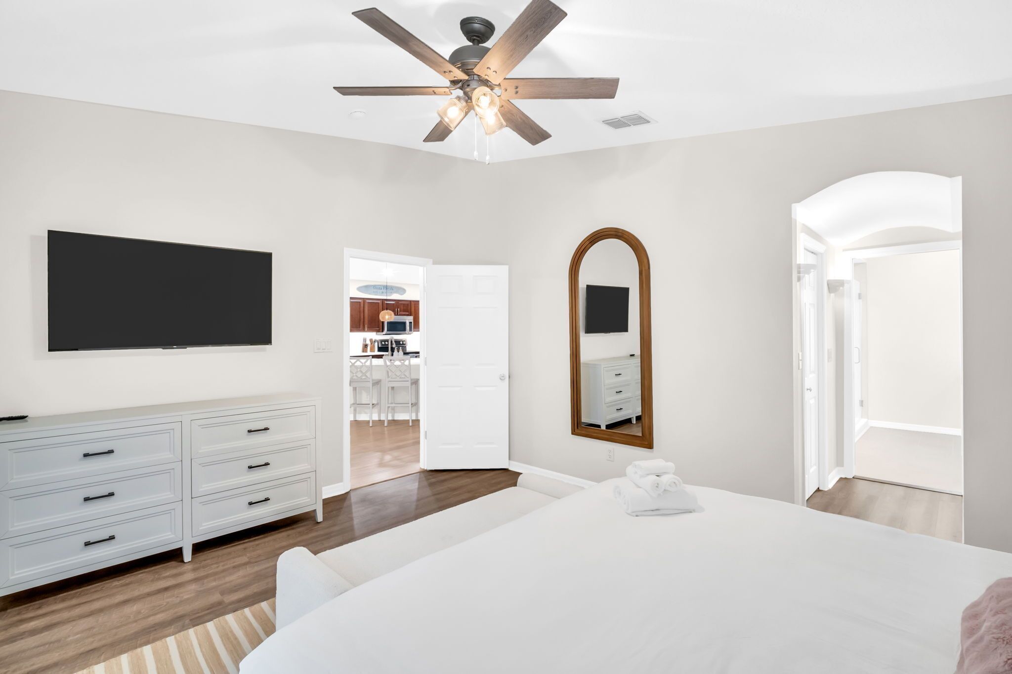 Une chambre à coucher moderne avec un grand lit, un ventilateur de plafond, une télévision, une commode et un dressing.