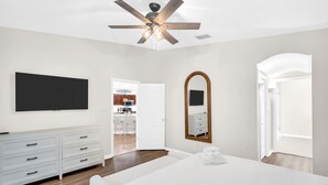 Ein modernes Schlafzimmer mit einem großen Bett, einem Deckenventilator, einem Fernseher, einer Kommode und einem begehbaren Kleiderschrank.