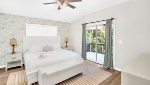 Ein Schlafzimmer mit einem großen Bett, einem Deckenventilator, einem Nachttisch mit Lampe und einer Schiebetür zum Balkon.