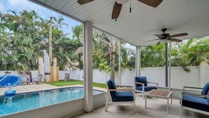 Ein überdachter Außenbereich mit Pool, blauen Stühlen und Deckenventilator.