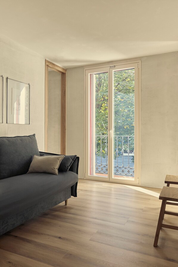 A modern living room with a grey sofa, a wooden coffee table, and a large sliding glass door leading to a balcony. - Enea Living (Bilbao)