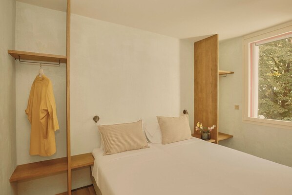 A bedroom with a bed, two pillows, a hanging robe, and a window with a view of trees. - Enea Living (Bilbao)