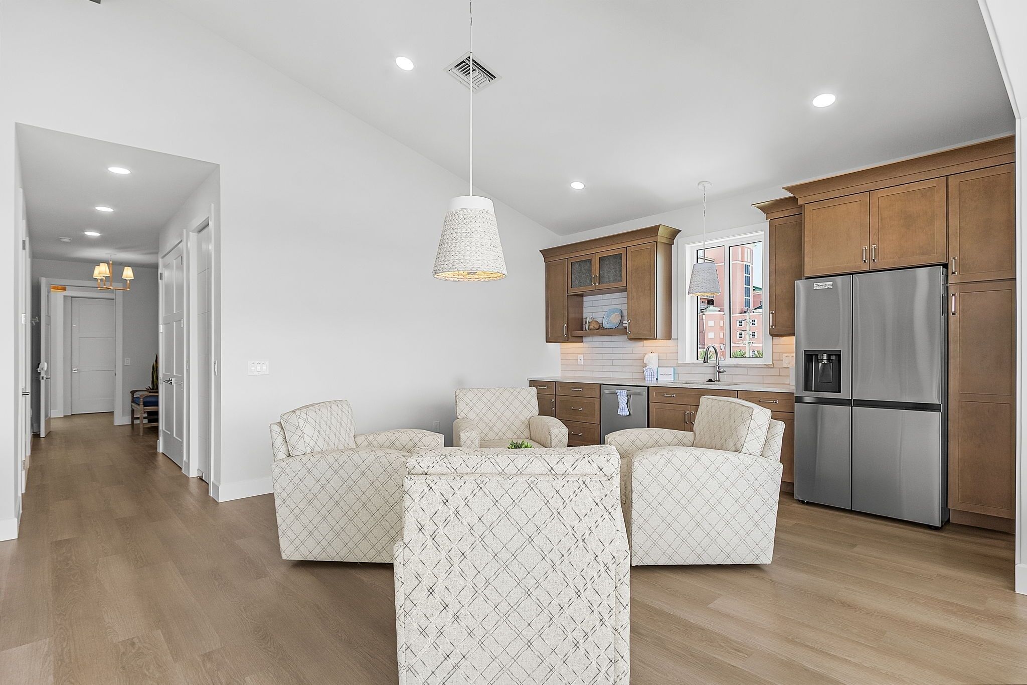 A modern kitchen with wooden cabinets, a stainless steel refrigerator, and a dining area with patterned chairs.