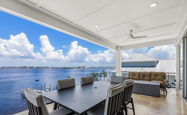 A spacious balcony with a view of the water and a bridge, a dining area with a table and chairs, and a seating area with a sofa.