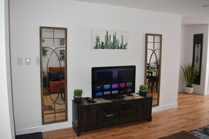 Un salon avec un téléviseur posé sur une console en bois foncé, un cactus et une œuvre d’art sur le thème des cactus accrochée au mur.