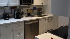 A modern kitchen with white cabinets, a stainless steel dishwasher, a microwave, and a coffee maker.