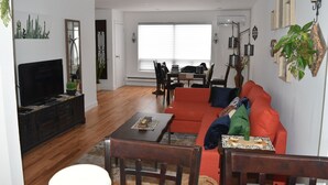 A living room with a flat-screen TV, wooden furniture, a red sofa, and a dining area with a table and chairs.