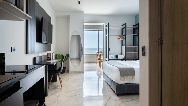 A modern bedroom with a large bed, a desk with a chair, a TV mounted on the wall, and a view of the ocean through an open door. - w Scenic 3BR w Ocean View Near C Amurallada (Cartagena)