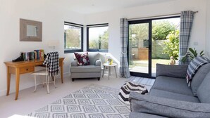 Ein modernes Wohnzimmer mit einer Couch, einem Schreibtisch und einem Sessel. Ein Fenster mit Vorhängen bietet einen Ausblick nach draußen.