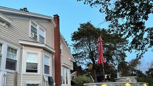 A two-story house with a stone wall and a red umbrella. - Bright 3BR House • New patio, Fire Pit, Outdoor Shower, EV Charger • Beach 4min (York)