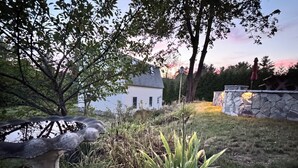 A garden with a stone sculpture, a white house, and a stone wall. - Bright 3BR House • New patio, Fire Pit, Outdoor Shower, EV Charger • Beach 4min (York)
