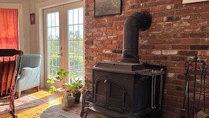 A cozy room with a brick fireplace, a wooden chair, and a potted plant. - Bright 3BR House • New patio, Fire Pit, Outdoor Shower, EV Charger • Beach 4min (York)