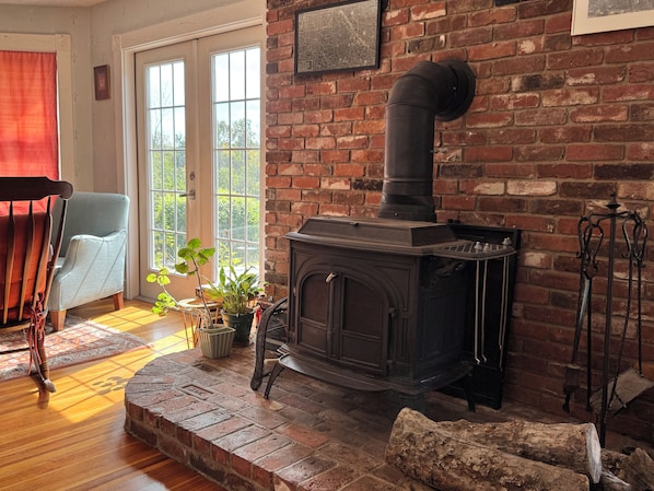 A cozy room with a brick fireplace, a wooden chair, and a potted plant. - Bright 3BR Coastal Home • Fire Pit, Outdoor Shower, EV Charger• Near York Harbor (York)