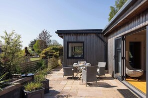 An outdoor patio with a table and chairs, surrounded by potted plants and a wooden fence.